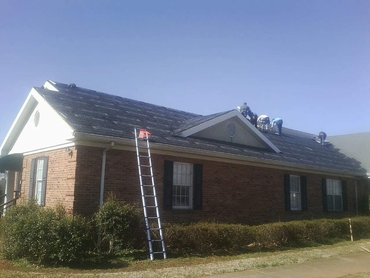 Crew tearing shingles off a brick ranch roof with a ladder set — Emergency Roof Repair work by our crew in Hiram