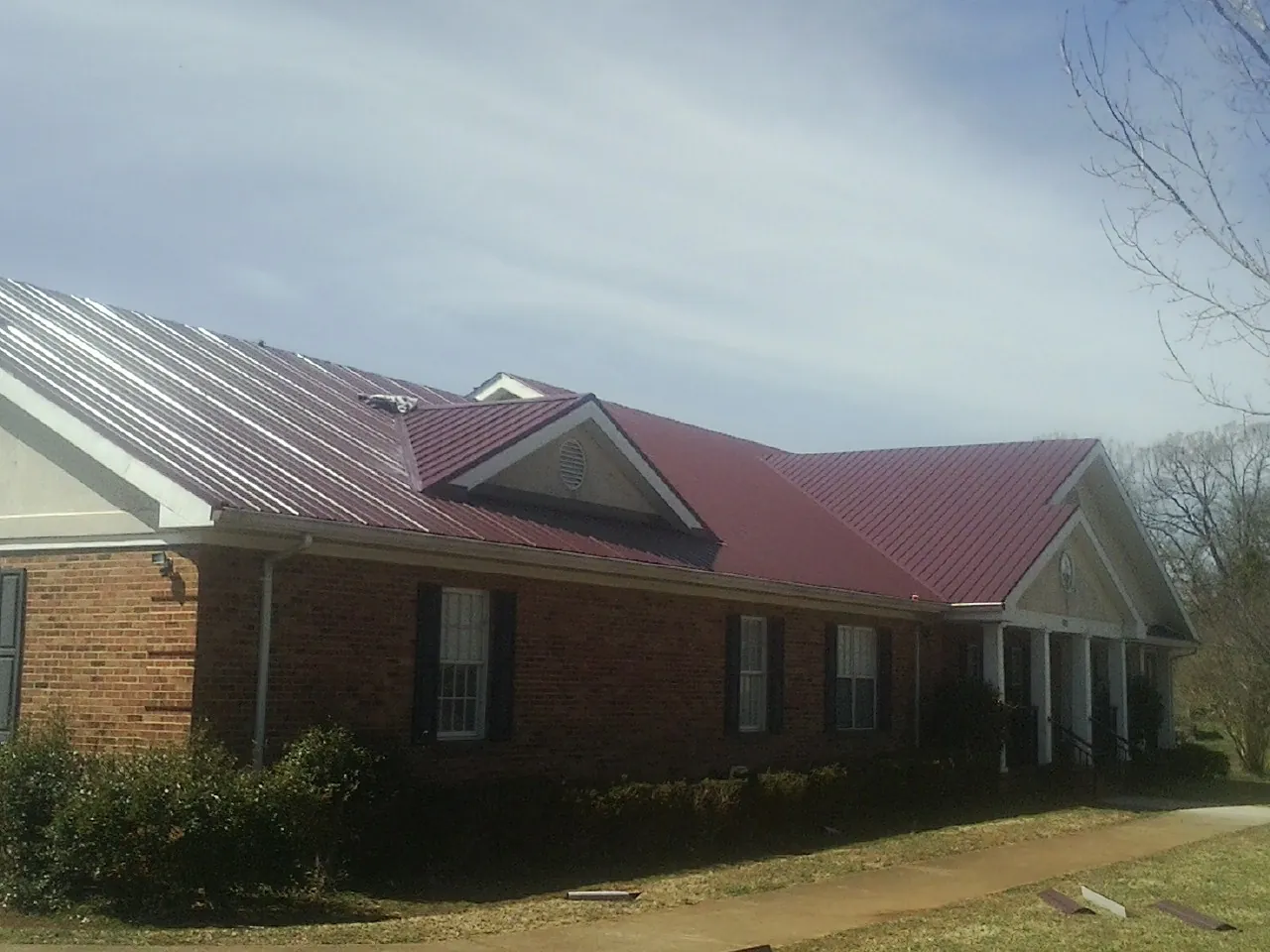 Red metal roof with gabled entries on a long brick building, from a Hail Damage Roof Repair job in Hiram